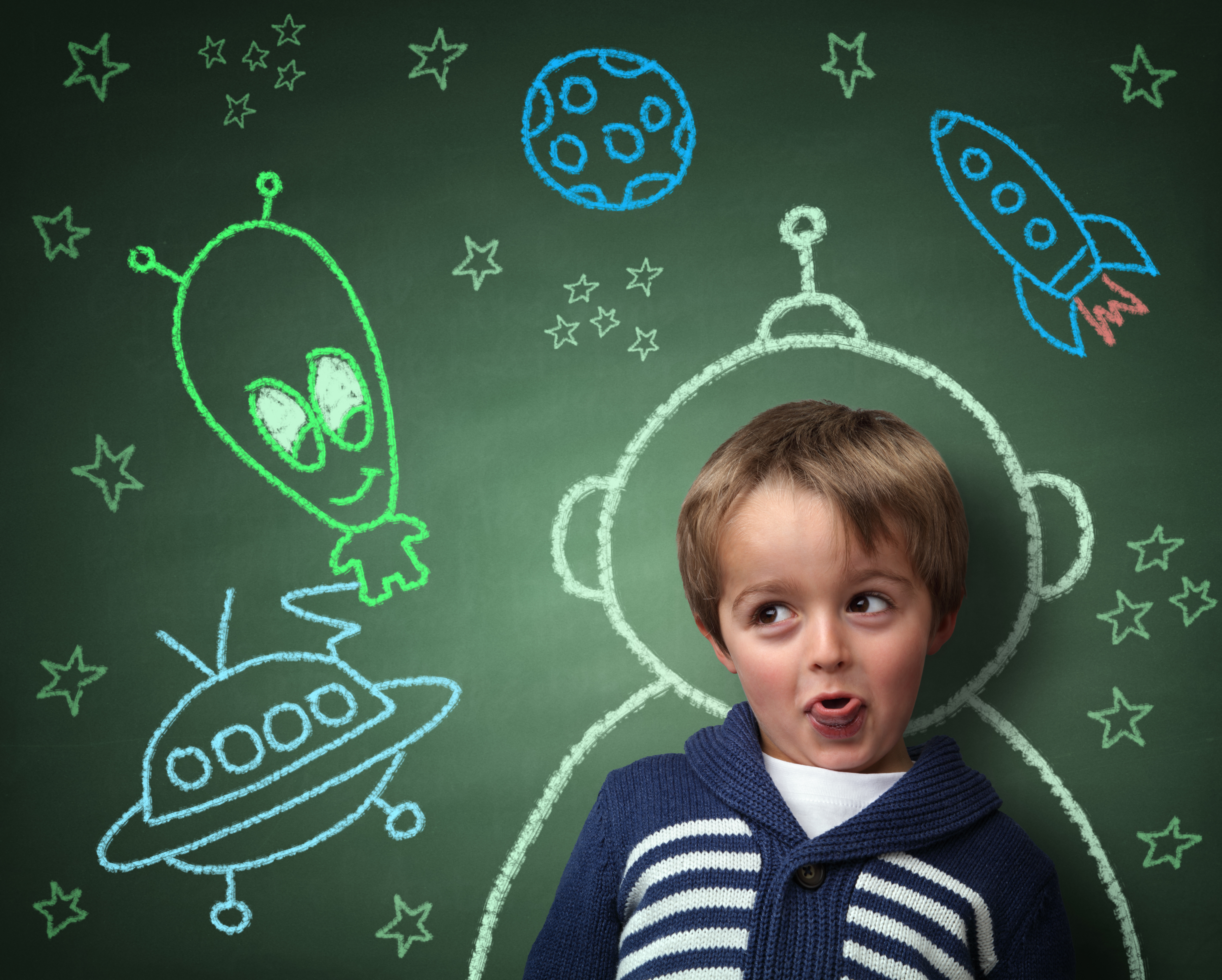 Imagination and dreams of a child, dressed as a space man in front of a blackboard with chalk drawings of space rocket and alien, concept for aspirations and daydreaming
