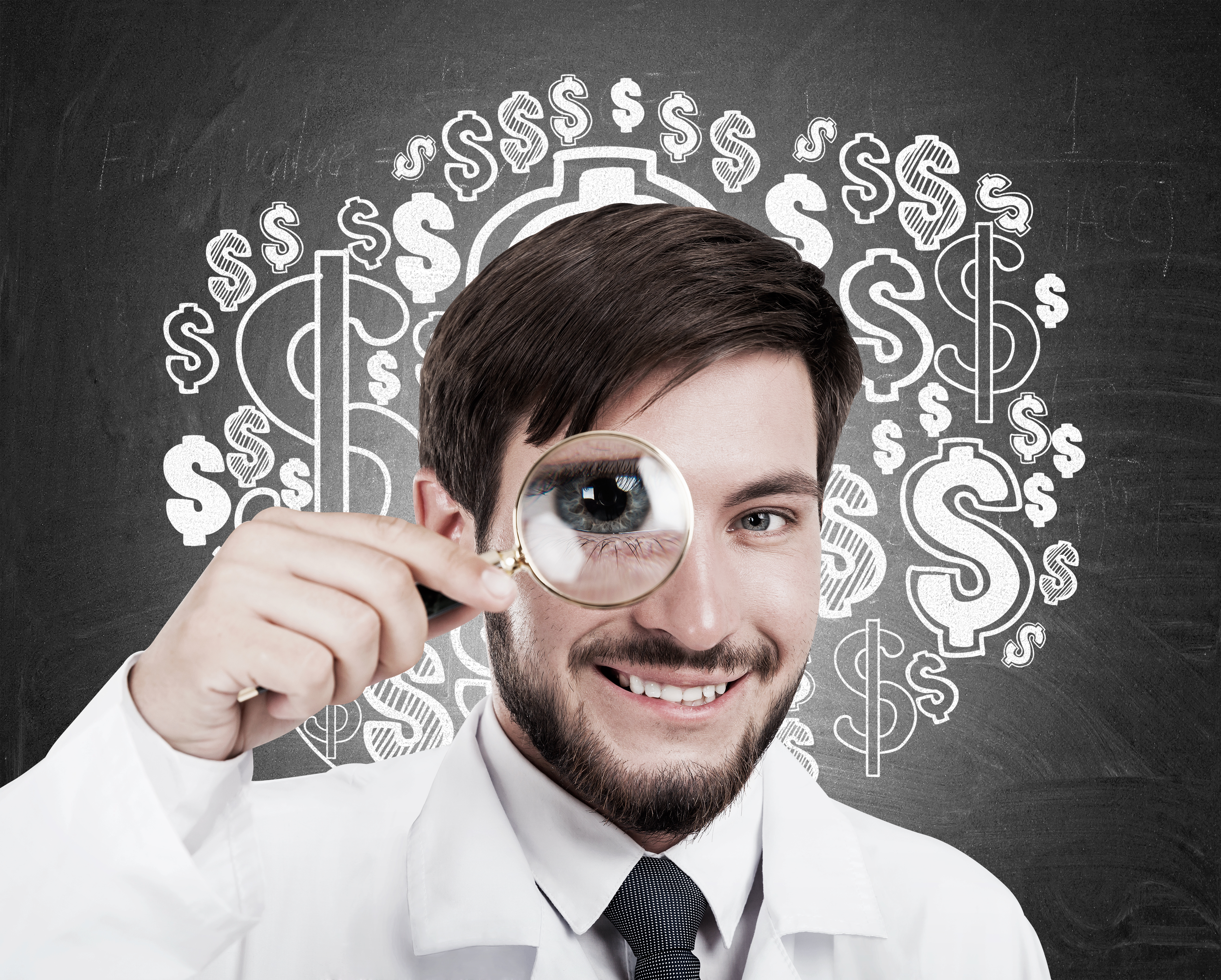 Smiling young doctor looking through magnifying glass standing against blackboard with dollar sketches on it. Concept of medical services
